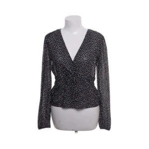 Svart prickig omlottblus med v-ringning - Svart blus med vita prickar och snygg omlott-design framtill. V-ringad hals och långa ärmar. 