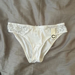 Vit spetsdetaljerad trosa - Snygg vit trosa med blommiga spetsdetaljer på sidorna och mjukt tyg framtill och baktill. Spetsen har små broderade blommor.helt oanvända med prislapp kvar, I storlek L/40. Köpta för 149kr säljer för 60kr .