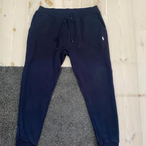Mörkblå mjukisbyxor från Polo Ralph Lauren - Snygga mörkblå mjukisbyxor från Polo Ralph Lauren med klassisk broderad logga i vitt på benet. Byxorna har snörning i midjan, ribbade muddar vid benslut och mjukt bomullsmaterial som är perfekt för chill eller träning. Fickor på sidorna för extra funktion.