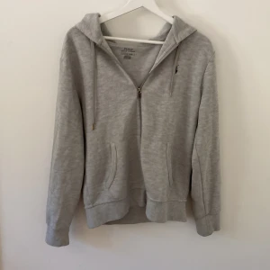 Grå hoodie från Polo Ralph Lauren - Säljer en ljusgrå hoodie från Polo Ralph Lauren med dragkedja och huva. Tröjan har snörning i huvan, två fickor fram och den klassiska Polo-loggan broderad på bröstet. Har älskat den här tröjan så länge men har knappt på den längre. Vet att många killar har den här men funkar på tjejer med!