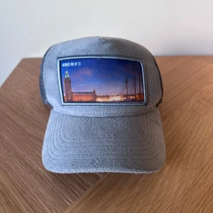 Grå keps från Revenite med stadsmotiv - Snygg grå keps från Revenite med ett coolt stadsmotiv framtill och mesh på baksidan för extra ventilation. Framsidan har en bild av Stockholms stadshus i kvällsljus. Perfekt för dig som gillar unik design och streetstyle eller en klassisk Stockholm stil.