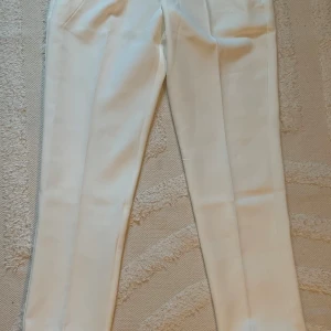 Vita kostymbyxor från Banlvdun - Helt ny. Snygga vita kostymbyxor från Banlvdun med pressveck och raka ben. Byxorna har diskreta bakfickor med knappar och är tillverkade i ett slätt tyg som ger en clean och stilren look. Perfekta för dig som vill ha en fräsch och dressad stil.