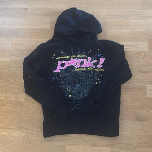 Sp5der Hoodie S - Cool svart hoodie med stor huva och färgglad print på bröstet. Trycket har en spindelnätsdesign, stjärnor i gult, blått och rosa samt texten 'nevermind the spider, heres the slime' i poppiga färger. Märkets gula stjärnlogo finns på ryggen. Perfekt för dig som gillar statement-plagg.