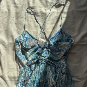 Blå paisleymönstrad sommarklänning - Säljer en flowy klänning med paisleymönster i blått, grönt och vitt. Klänningen har smala axelband som korsas i ryggen.