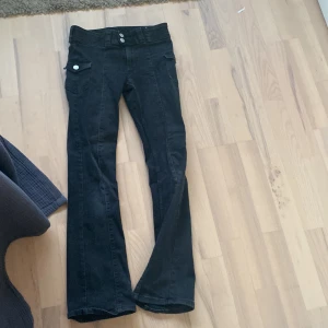 Svarta bootcut jeans - Snygga svarta bootcut jeans med hög midja och knappar fram. Perfekta för en stilren look. De har en ficka med knappdetalj på sidan och är tillverkade i ett stretchigt material för extra komfort.