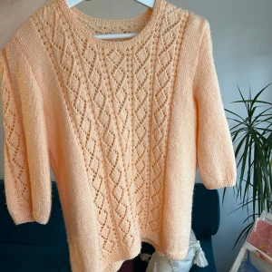 Persikofärgad stickad tröja - Säljer en söt persikofärgad handstickad tröja i ull med ett vackert hålmönster framtill. Tröjan har trekvartsärmar och en rund halsringning. Perfekt för en mysig dag ute eller hemma. 🌸xs-s