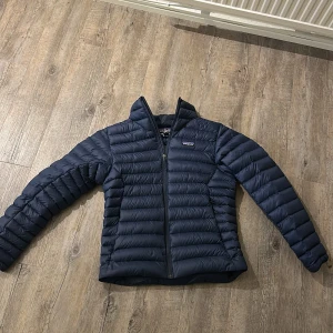 Blå dunjacka från Patagonia - Säljer en snygg mörk blå dunjacka från Patagonia. Jackan har en dragkedja framtill  Perfekt för vår och höst dagar skulle jag säga. Den köptes förra året och är använd max 10 gånger. Köpte den för 3000. Har tappat bort kvittot. Priset kan diskuteras. Hör av dig ifall du undrar något eller skriv privat om flera bilder.