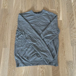 Grå tröja från H&M - Grå slim fit tröja från H&M. Tröjan har långa ärmar och är tillverkad i en mjuk bomull och tyg blandning fast som är lite tjockare. Storlek S