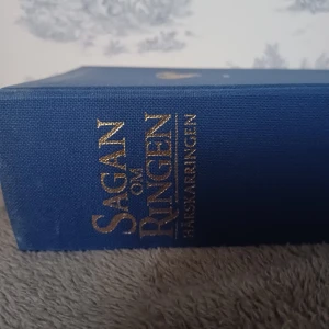 Sagan om Ringen - En vacker blå inbunden bok med guldtext på ryggen och en gyllene drake på framsidan. Boken innehåller illustrationer och är en del av en klassisk fantasyserie.