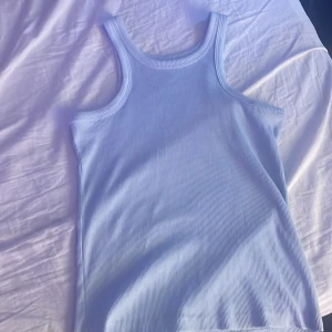 Ljusblå ribbad linnetopp - Säljer en stilren ljusblå ribbad linnetopp. Perfekt för varma dagar med sin ärmlösa design och mjuka material. Ett måste i garderoben för en avslappnad look.