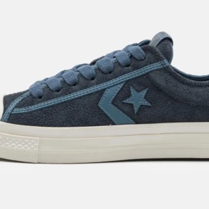 Blå sneakers från Converse - Snygga blå sneakers från Converse i mocka med den klassiska stjärnloggan på sidan. Skorna har en vit sula och matchande blå snörning. Perfekta i vår. Helt oanvända och kvar i förpackningen!