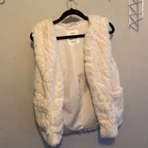 Vit pälsväst från Zara Kids - Säljer en fluffig och stilren vit pälsväst från Zara Kids. Den har en mjuk insida och är en del av deras outerwear collection. Aldrig andvänd💘
