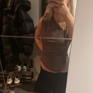 Brun ärmlös topp från Zara - Säljer en snygg brun ärmlös topp från Zara med omlott-design och knytning i sidan. Perfekt för en stilren look. Passar bra till både jeans och kjol. Använd 1 gång. 