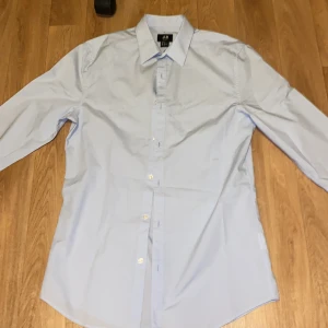 Ljusblå skjorta Helt ny - Säljer en stilren ljusblå skjorta från H&M i slim fit. Skjortan har långa ärmar och knappar framtill. Perfekt för en snygg och enkel look. Och helt ny