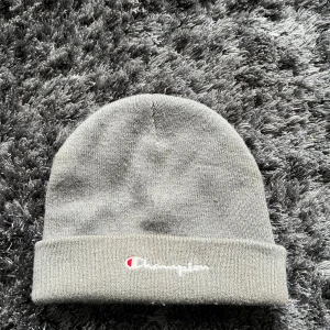 Grå mössa från Champion - Snygg grå mössa från Champion med broderad logga framtill. Perfekt för kyliga dagar och en stilren look.