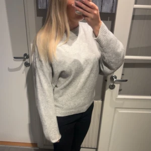 Grå stickad tröja - Säljer en mysig grå stickad tröja med normal passform. Tröjan har långa ärmar och en rund halsringning, perfekt för kyligare dagar. Den är enkel och stilren, vilket gör den lätt att matcha med olika outfits.