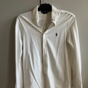Ralph Lauren skjorta - Säljer en stilren vit långärmad skjorta från Ralph Lauren. Skjortan har en liten defekt som bara syns på nära håll och når man han en t shirt i annan färg under, syns på sista bilden 