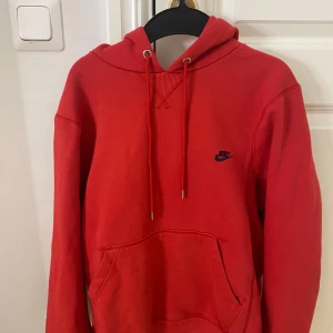 Röd hoodie från Nike - Säljer en snygg röd hoodie från Nike med klassisk känguruficka och justerbar huva. Perfekt för en avslappnad stil. Den har en liten Nike-logga på bröstet.