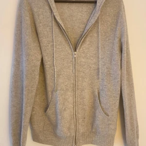 Grå kashmir hoodie från John Henric - Säljer en lyxig och mjuk grå hoodie i kashmir från John Henric. Tröjan har en dragkedja framtill och praktiska fickor. Perfekt för kyliga dagar med sin sköna passform och stilrena design. Hör av dig vid intresse! Kostar 3000kr nypris och har litet hål vid luvan, inget som märks alls när man har på sig den!