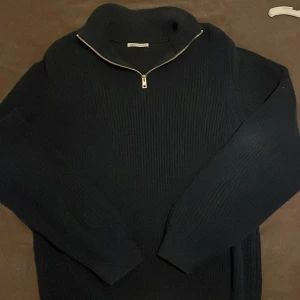 Mörkblå stickad tröja från Zara - Säljer en stilren mörkblå stickad tröja från Zara med dragkedja vid halsen. Perfekt för kyliga dagar med sin mjuka och bekväma passform. Tröjan har långa ärmar och en ribbad struktur som ger en klassisk look.