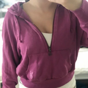 Rosa hoodie från Victoria's Secret - Säljer en snygg rosa hoodie från Victoria's Secret med dragkedja och känguruficka. Perfekt för en avslappnad stil. Hoodien har långa ärmar och en justerbar huva med snören.
