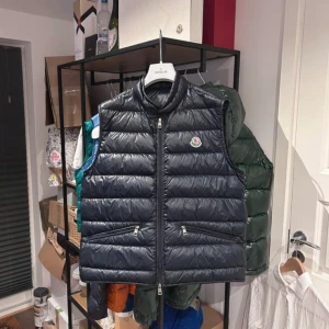 Svart dunväst från Moncler - Snygg svart dunväst från Moncler med dragkedja och två fickor framtill. Västen har en quiltad design och Moncler-loggan på bröstet. Perfekt för kyligare dagar. byten tillgänglig 💫