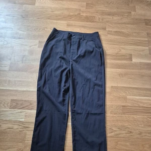 Svarta tunna kostymbyxor - Snygga svarta kostymbyxor med hög midja och rak passform. Perfekta för en stilren look. Byxorna har en knapp och dragkedja framtill.