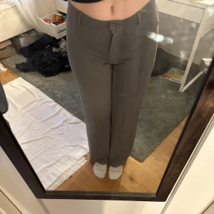 Grå kostymbyxor - Snygga grå kostymbyxor med hög midja och rak passform. Byxorna har en knapp och dragkedja framtill samt hällor för bälte. Perfekta för en stilren look. I modellen keep it up low waist kostymbyxor.