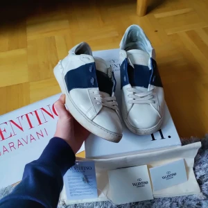 Valentino Garavani sneakers i vitt och blått - Feta Valentino opens! Färg: vit och navy blue! Storleken är 44 skick 8.5/10 vad följer med? Box, dustbag, bag, kuvert, kort och prislapp! Självklart äkta! hör av er vid minsta fundering! Byten kan vara intressant🤩