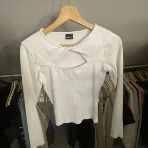 Vit ribbad topp från Gina Tricot - Säljer en stilren vit ribbad topp från Gina Tricot. Toppen har en unik detalj vid halsringningen och långa ärmar. 