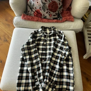 Rutig skjorta från H&M - Säljer en snygg rutig skjorta från H&M i gröna, svarta och beige toner. Skjortan har långa ärmar och knappar framtill. Perfekt för en avslappnad stil.