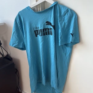 Blå t-shirt med Puma-tryck - Säljer en blå t-shirt med ett coolt 'I like Puma' tryck på framsidan. T-shirten har korta ärmar och en avslappnad passform. Perfekt för en casual look eller träning. 🐾