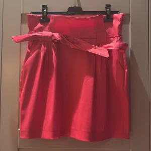 Rosa kjol med knytband - Snygg rosa kjol med hög midja och knytband. Kjolen har en kort längd och två fickor baktill. Perfekt för en färgglad look!