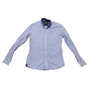 Blå skjorta från Hampton Republic - Snygg blå skjorta från Hampton Republic i regular fit. Skjortan har långa ärmar och knappar framtill. Perfekt för en stilren look.