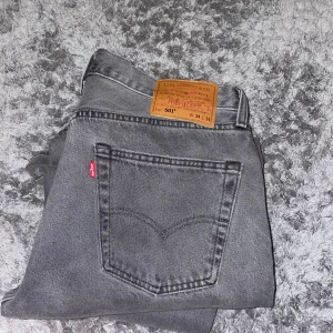 Grå Levis 501 jeans - Snygga grå Levis 501 jeans med klassisk design och rak passform. De har en ikonisk läderlapp baktill och en röd etikett på bakfickan. Perfekta för en stilren look. 34 x 34