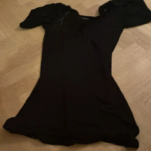 Svart klänning från mbyM - Snygg svart klänning från mbyM med puffiga kortärmar och knytning framtill. Perfekt för en stilren look. Klänningen har en elegant passform och är tillverkad i ett mjukt material. Ganska genomskinlig