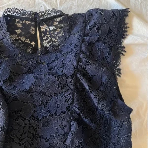 Mörkblå spetsblus från Zara - Snygg mörkblå spetsblus från Zara med blommigt mönster. Blusen är ärmlös och har en elegant design med volangdetaljer. Perfekt för att ge en stilfull touch till din outfit.