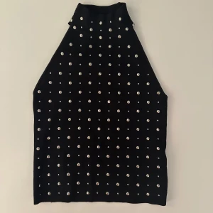 Svart ärmlös topp med pärlor - Snygg svart ärmlös topp dekorerad med pärlor över hela ytan. Toppen har en hög hals och ger en elegant look.