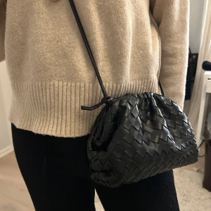 Svart flätad axelväska - Snygg svart axelväska med flätat mönster och justerbar axelrem. Väskan är nästan aldrig använd och den är köpt i Köpenhamn så kommer tyvärr inte ihåg märket💕💕
