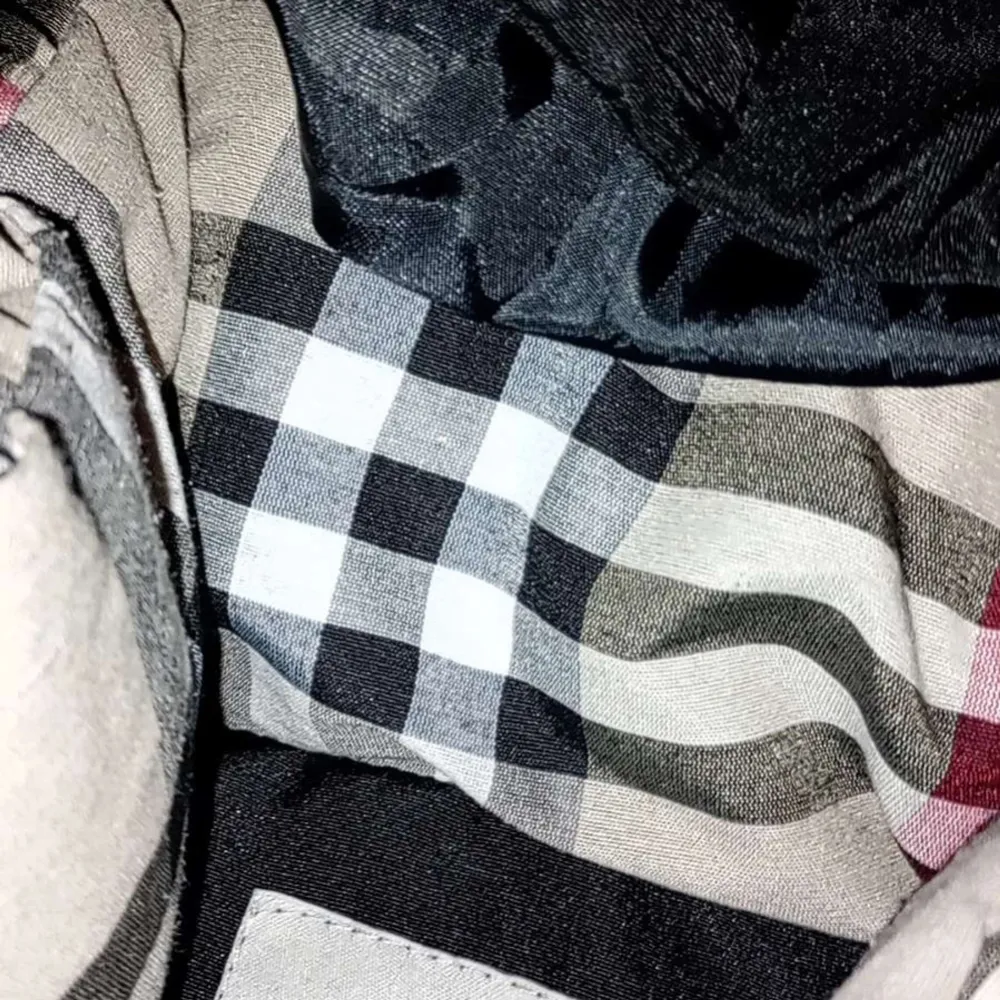 Snygg svart dunjacka från Burberry med det ikoniska TB-monogrammet broderat på bröstet. Jackan har en klassisk rutig insida i svart, vitt och rött. Perfekt för kyliga dagar med stil.. Takit.