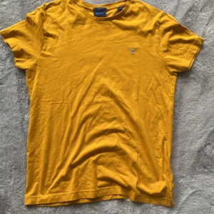 Orange t-shirt från GANT - Säljer en snygg gul t-shirt från GANT i storlek S. Den har en broderad logga på bröstet och är tillverkad i mjuk bomull. Perfekt för en avslappnad stil. Varsamt använd passar även M