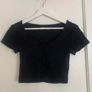 Svart ribbad kortärmad topp - Säljer en stilren svart ribbad topp med korta ärmar och knappar där fram. Superfint skick och använd fåtal gånger. 