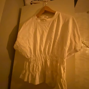 Vit blus med resår i midjan - Säljer en söt vit blus med resår i midjan som ger en fin passform. Blusen har korta ärmar och en rund halsringning. Perfekt för en avslappnad stil.