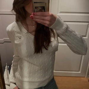 Vit GANT tröja🤍 - Säljer en stilren vit kabelstickad tröja från GANT i stretchig bomull. Tröjan har en v-ringad hals och långa ärmar, perfekt för en klassisk look. 