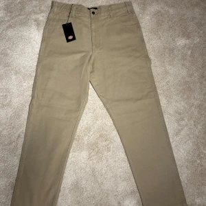 Dickies - Snygga beige cargopants från Dickies med praktiska fickor och en klassisk design. Perfekta för en avslappnad stil. Byxorna har en dragkedja och knapp i midjan.