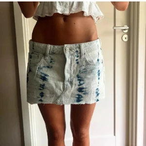 Jeanskjol med batikmönster - Trendig jeanskjol med blått batikmönster. Kort modell med klassisk femficksdesign och knappgylf. Perfekt för en avslappnad stil.