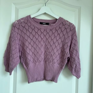 Lila stickad tröja från Bik Bok - Säljer en söt lila stickad tröja från Bik Bok. Tröjan har ett fint hålmönster och är croppad med trekvartsärmar. Perfekt för en stilren look!