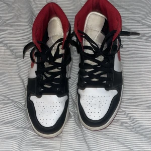 Nike Air Jordans i svart, vitt och rött - Säljer ett par klassiska Nike Air Jordans i svart, vitt och rött. Skorna har snörning och en ikonisk design med hög krage. Perfekta för dig som älskar sneakers med stil.