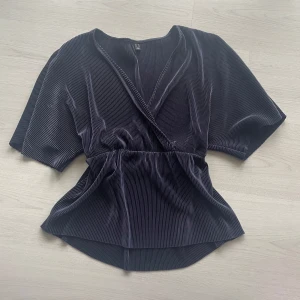 Marinblå omlottopp från Vero Moda - Snygg marinblå blus med stretch band i midjan med bra kvalite, den är lite glansig vilket gör den mer unik, kan ha till tjejkväller eller en fina blus på en fredag!!