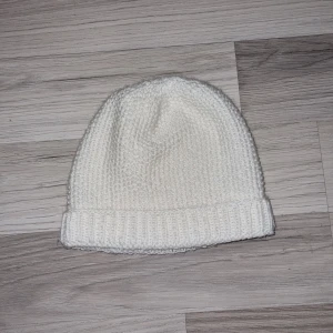 Vit stickad mössa - Säljer en stilren vit stickad mössa med ribbad kant. Perfekt för att hålla värmen under kyliga dagar. Mössan har en klassisk design som passar till det mesta. Hemmastickad 